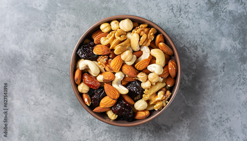 Various dried fruits and nuts in a ceramic bowl (walnut, cashew, almonds, pine nuts, hazelnuts) on a gray stone or slate background. The concept of a healthy dessert. Flat lay, top view. Various dried fruits and nuts in a ceramic bowl (walnut, cashew, almonds, pine nuts, hazelnuts) on a gray stone or slate background. The concept of a healthy dessert. Flat lay, top view.