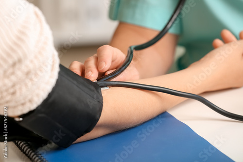 Female doctor measuring patient's blood pressure in clinic, closeup