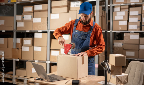 Bild auf Leinwand Warehouse male worker packing shipping ecommerce box checking website retail order preparing delivery parcel on table