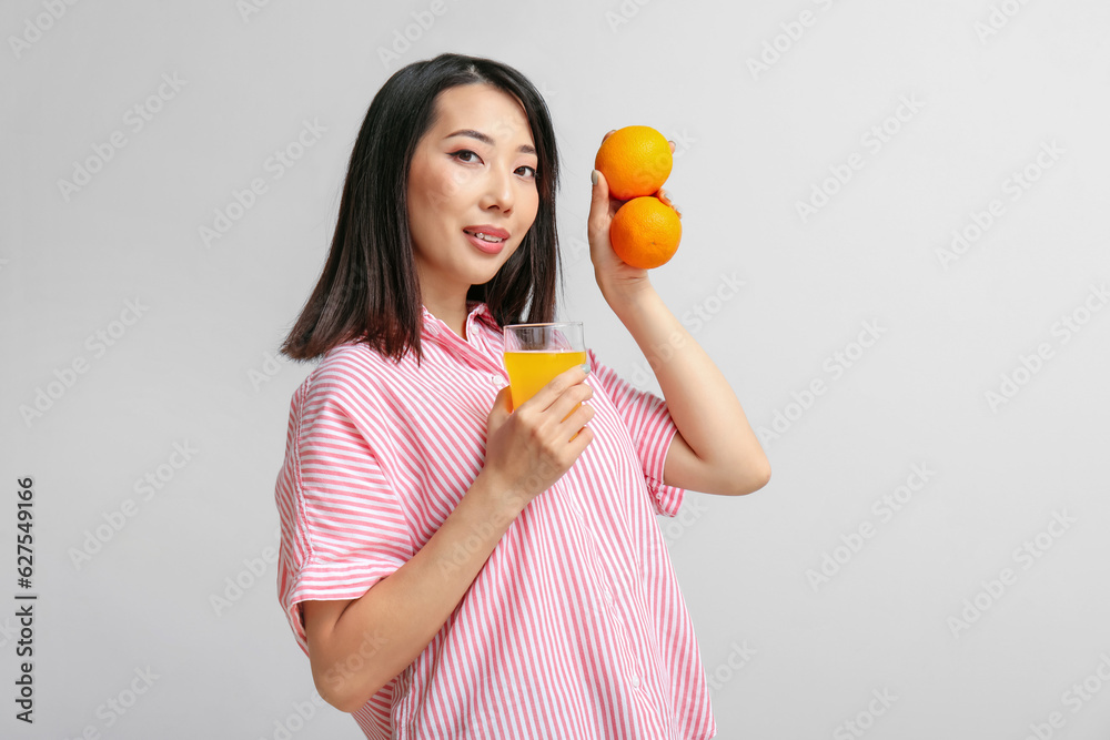 Beautiful Asian woman with oranges and glass of juice on light background Beautiful Asian woman with oranges and glass of juice on light background