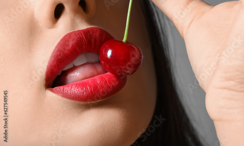 Beautiful woman with red lips and cherry on dark background, closeup photo