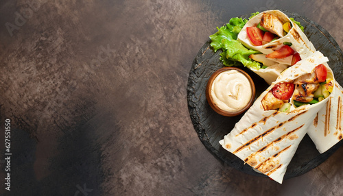 Shawarma pita bread with grilled chicken, fresh vegetables and cream sauce on a background of brown stone. Top view with copy space. photo