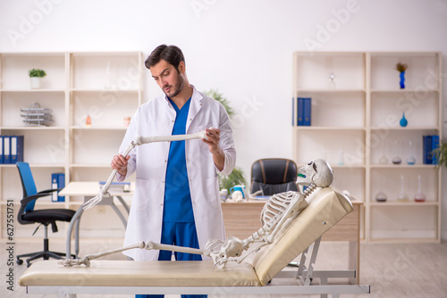 Young male doctor with skeleton in the clinic