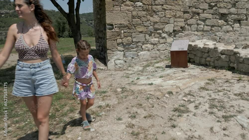 Reveal of three females walking towards chain fence and building ruins Reveal of three females walking towards chain fence and building ruins