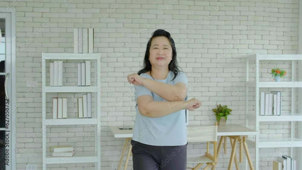 Morning work-out, Senior asian woman doing fitness exercises from home, Fitness woman doing stretch exercise stretching her arms, Elderly woman living an active lifestyle. Morning work-out, Senior asian woman doing fitness exercises from home, Fitness woman doing stretch exercise stretching her arms, Elderly woman living an active lifestyle.