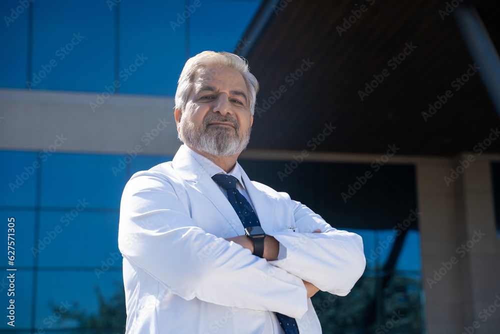 Confident Indian senior doctor standing in front of hospital Confident Indian senior doctor standing in front of hospital