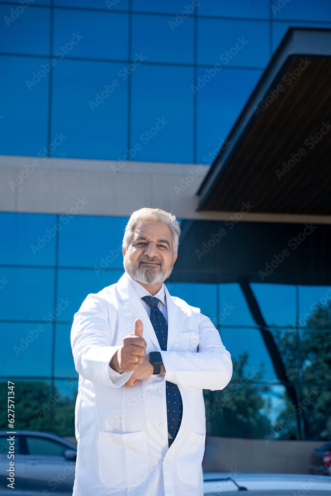 Fototapeta premium Senior doctor standing in front of hospital and showing thumps up