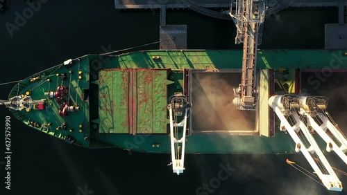 Aerial view fom above - wheat loading to bulker ship cargo hold at sea grain elevator in sea port. Wheat shipment from silo to vessel via moving trunk at a sea port terminal. Maritime transport. photo