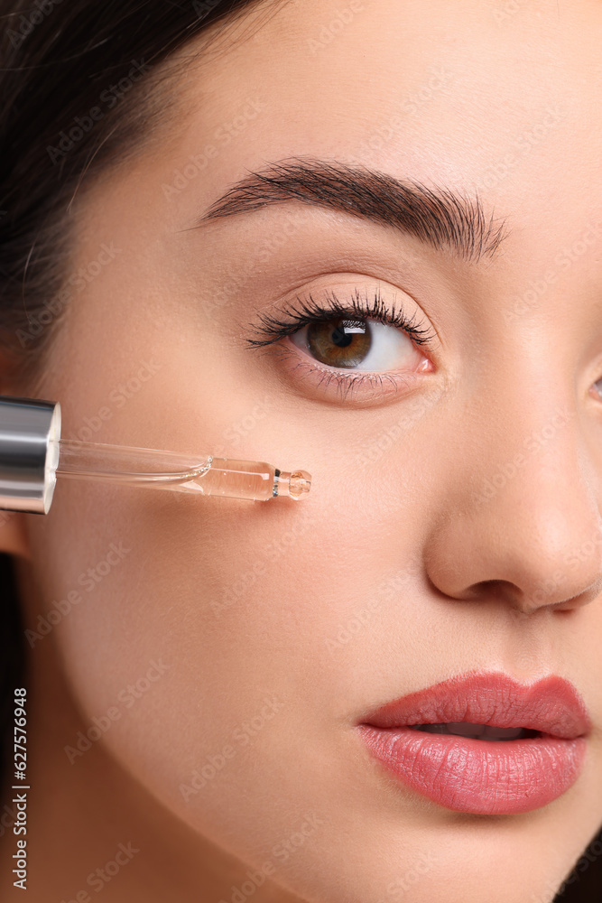 Young woman applying essential oil onto face, closeup