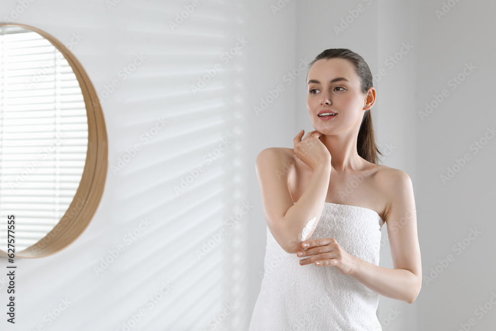 Beautiful woman applying body cream onto elbow in bathroom, space for text Beautiful woman applying body cream onto elbow in bathroom, space for text