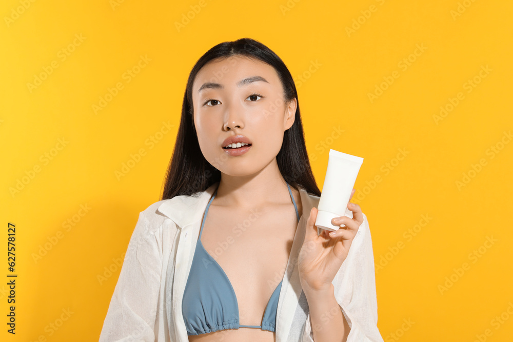 Beautiful young woman holding sun protection cream on orange background Beautiful young woman holding sun protection cream on orange background