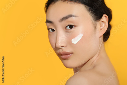 Beautiful young woman in sunlight with sun protection cream on her face against orange background, closeup. Space for text photo