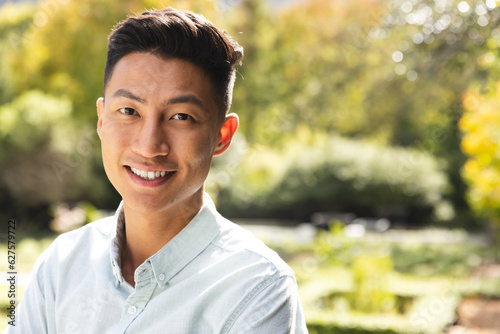Portrait of happy asian man smiling in sunny garden, copy space