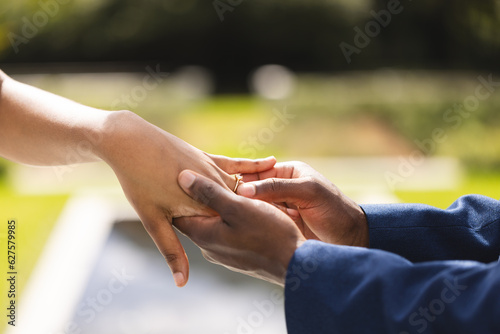 Hands of african american bride and groom placing ring on finger at wedding ceremony in sunny garden © WavebreakMediaMicro