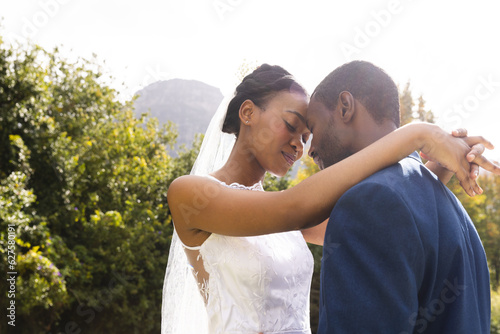 Happy african american bride and groom embracing at wedding in sunny garden