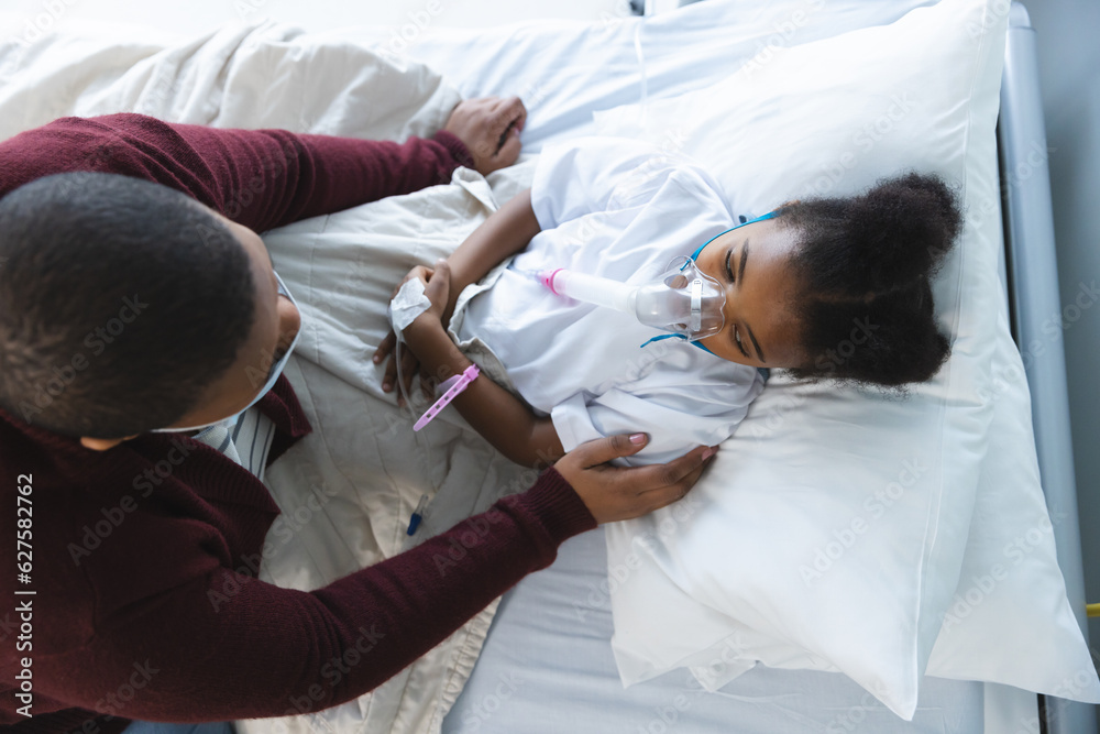 Obraz premium African american girl patient lying on bed with oxygen mask, with her mother at hospital