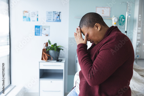 Sad african american female patient sitting on bed and crying in patient room at hospita, copy space