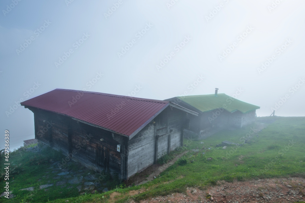 Highland landscape in cloudy and foggy weather. Highland houses made of stone and wood. Wooden plateau houses built on the hill. Wooden plateau houses in Turkey. Pokut Plateau Rize Türkiye.