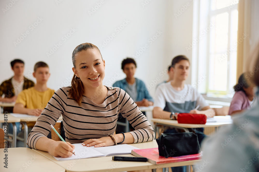 Happy female high school student taking notes during class and looking at camera. Happy female high school student taking notes during class and looking at camera.