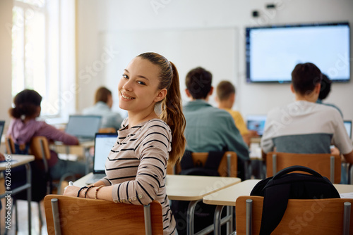 Happy teenage girl during IT class at high school looking at camera.