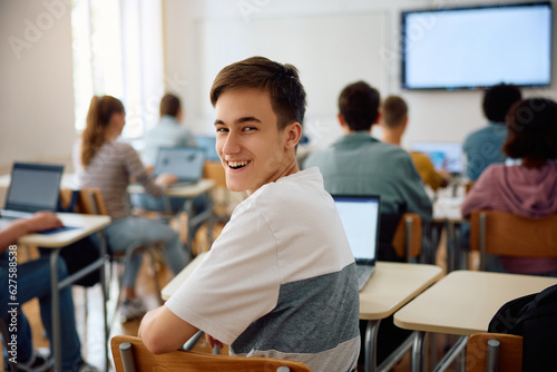 Happy high school student attending computer class in classroom and looking at camera.