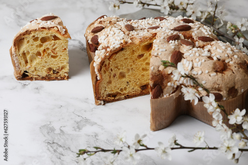 Delicious Italian Easter dove cake (traditional Colomba di Pasqua) and flowers on white marble table, closeup