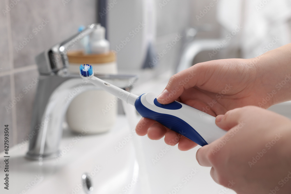 Woman holding electric toothbrush near sink in bathroom, closeup