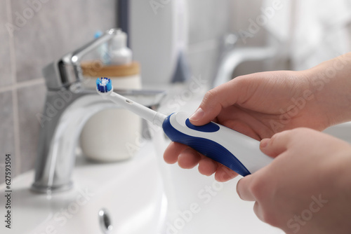 Woman holding electric toothbrush near sink in bathroom, closeup © New Africa