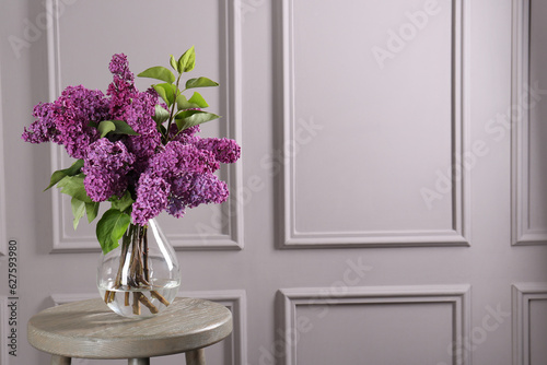 Beautiful lilac flowers in vase on wooden table near light wall  space for text