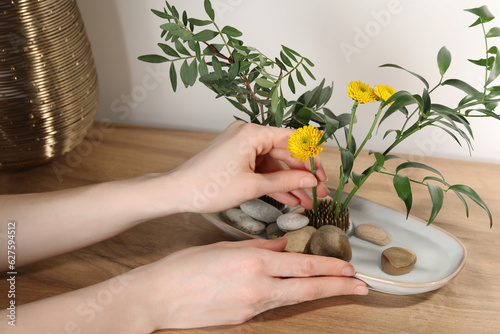 Woman creating stylish ikebana with beautiful flowers and green branches at table  closeup