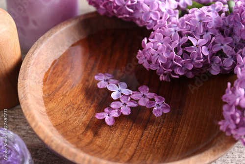 Bowl of water and lilac flowers on wooden table, closeup