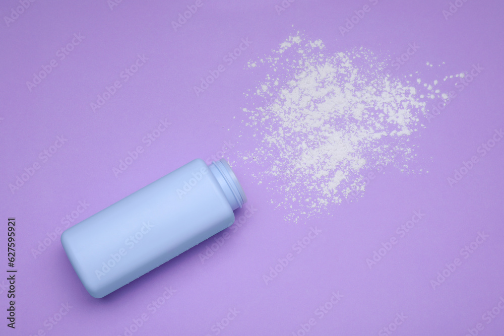 Bottle and scattered dusting powder on violet background, top view. Baby cosmetic product Bottle and scattered dusting powder on violet background, top view. Baby cosmetic product