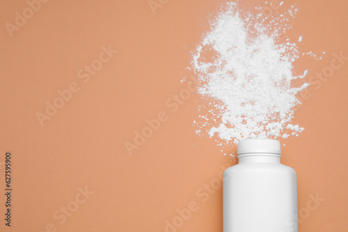 Canvas Print Bottle and scattered dusting powder on pale coral background, top view with space for text