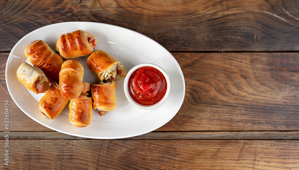 Delicious homemade sausage rolls on a white oval platter with tomato sauce on a wooden rustic table, finger food, english cuisine, view from above, flatlay, copy space