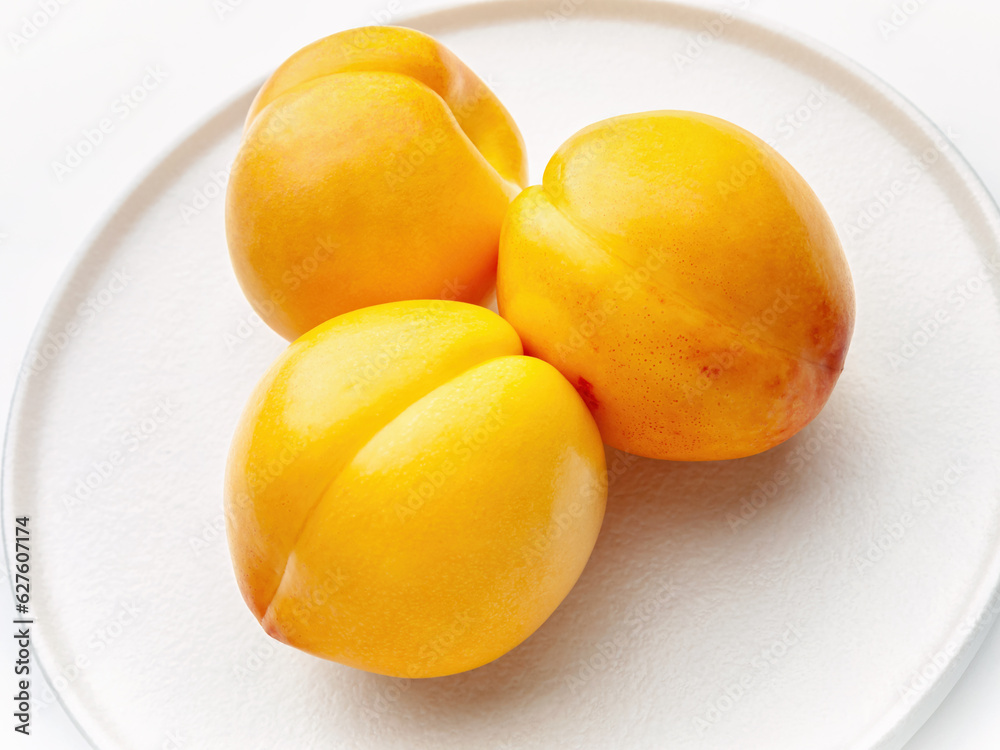 Three bright yellow nectarines on a white round plate, top and side view. Close-up. Horizontal.