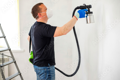 Worker in protective mask painting wall with spray gun