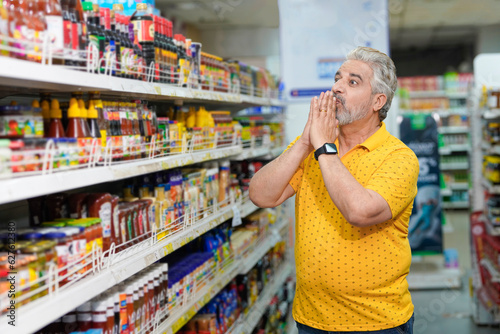 Slika na platnu Senior indian man shocking expression on inflation at grocery shop