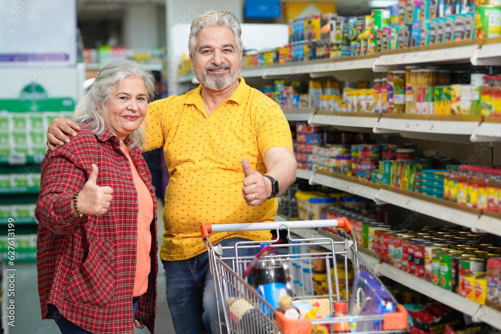 Senior indian couple showing thumps up while purchasing together at grocery shop.