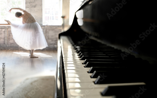A young ballerina in a white tutu rehearses a dance against the background of a grand piano in a vintage interior