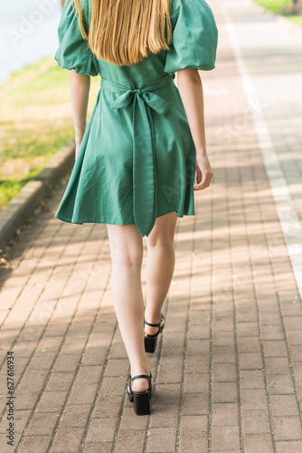 Close-up of women's legs. A girl walks in a green dress in the park in summer.