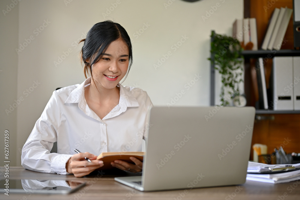 A beautiful Asian businesswoman focuses on her work on laptop at her desk in the office. A beautiful Asian businesswoman focuses on her work on laptop at her desk in the office.