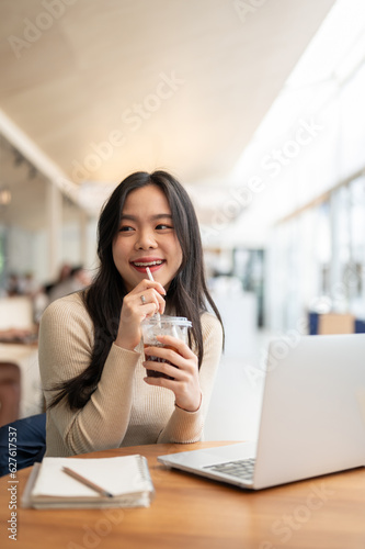 A charming Asian woman enjoying her iced coffee while working remotely at a coffee shop