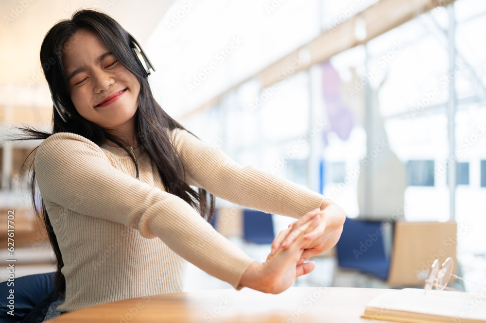 A pretty Asian woman enjoys the music and stretches her arms while relaxing at a table A pretty Asian woman enjoys the music and stretches her arms while relaxing at a table