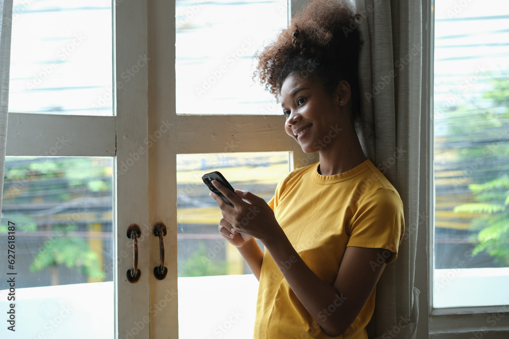 Delighted woman with Afro haired checking social media, chatting online on smartphone