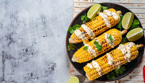 Elotes, Grilled Mexican Street Corn, charred cobs are covered in creamy mayonnaise, seasoned with chili powder and sprinkled with cheese, cilantro, and a spritz of lime juice, flat lay, free space photo