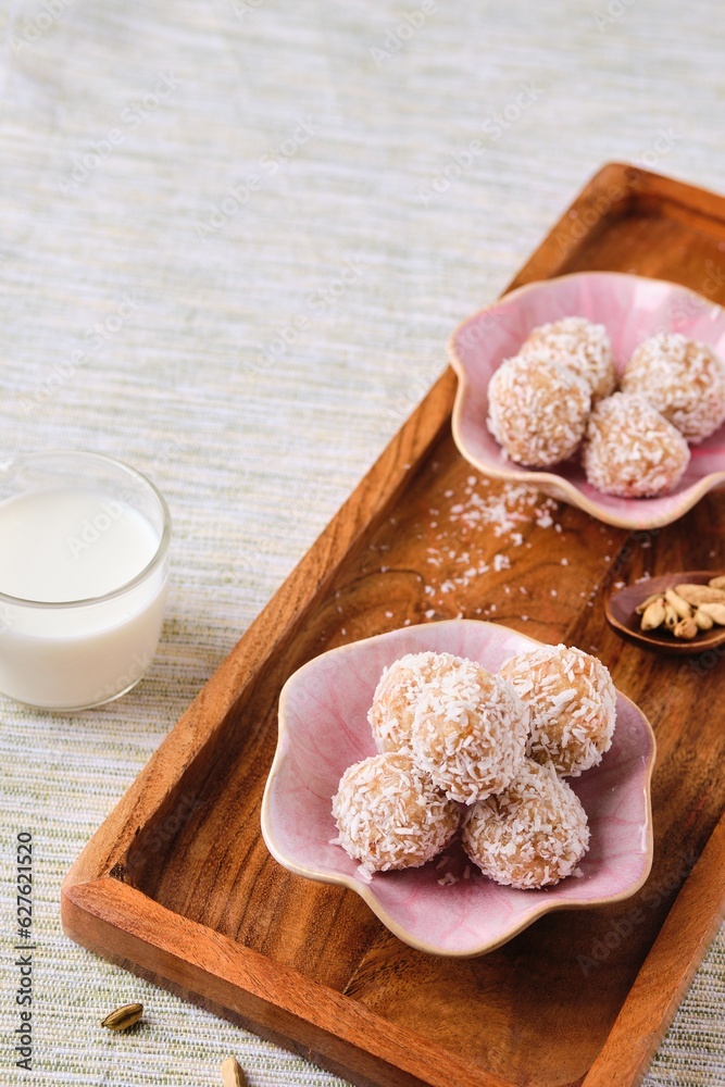 Handmade sweets, Laddu Indian sweet made from coconut, sugar and milk on a pink plate on a wooden tray. Vegan desserts, Vedic cuisine. Indian food