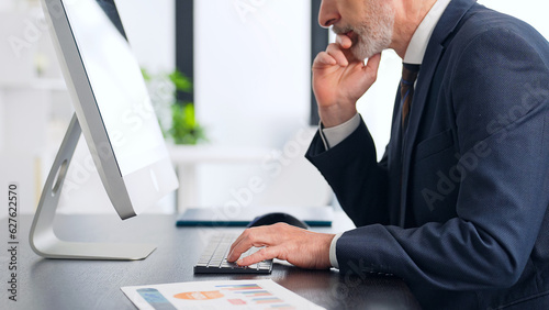 Middle-aged white man in a suit working in the office with desktop PC.