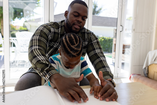 Sight impaired african american father and son practicing reading braille together at home