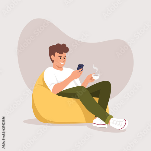 a man sits on an armchair (bean bag) with a phone and a cup of coffee