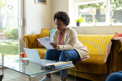 Plus size african american woman doing paperwork and using laptop at home